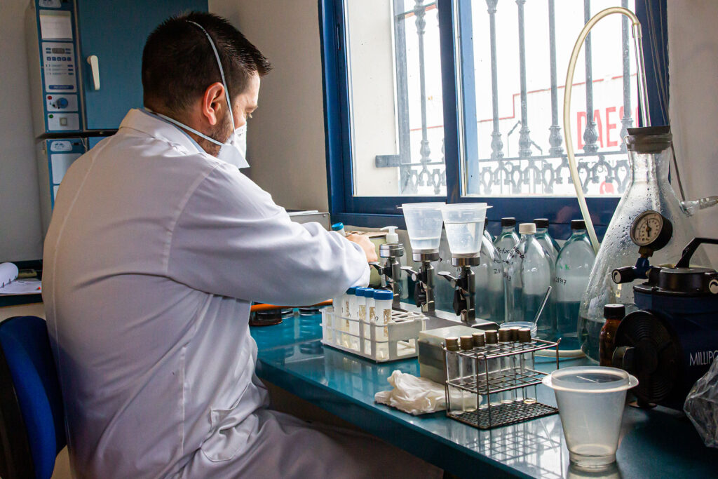 Científico con mascarilla en laboratorio observando funcionamiento de herramientas para análisis de agua.