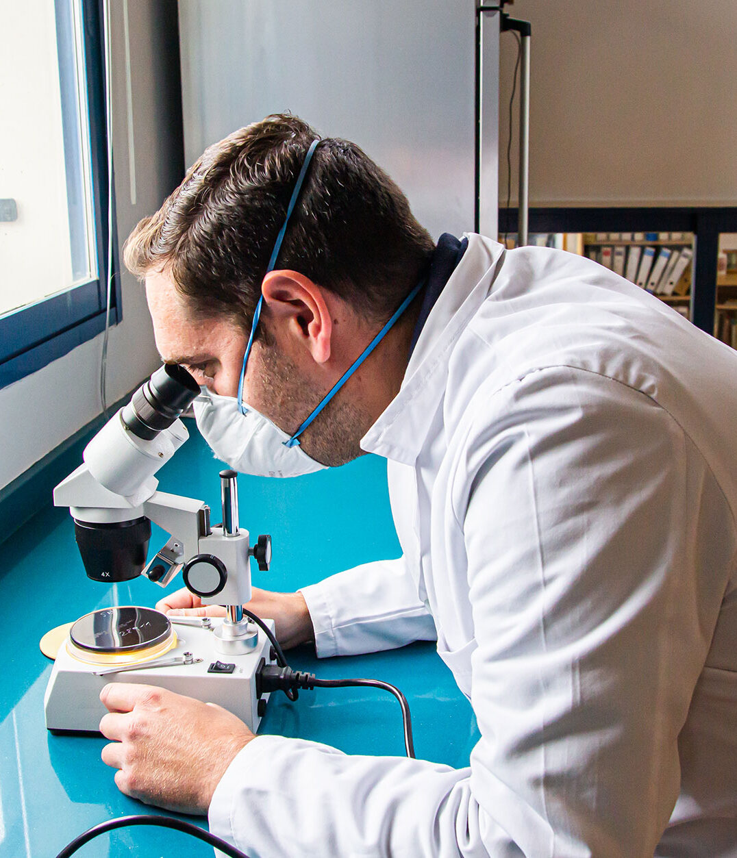 Científico con mascarilla mirando una muestra en un microscopio.